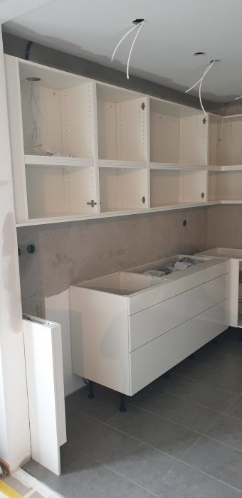 Nyinstallerade vita köksskåp och bänkskåp i ett renoveringsprojekt, ännu inte färdigställt.