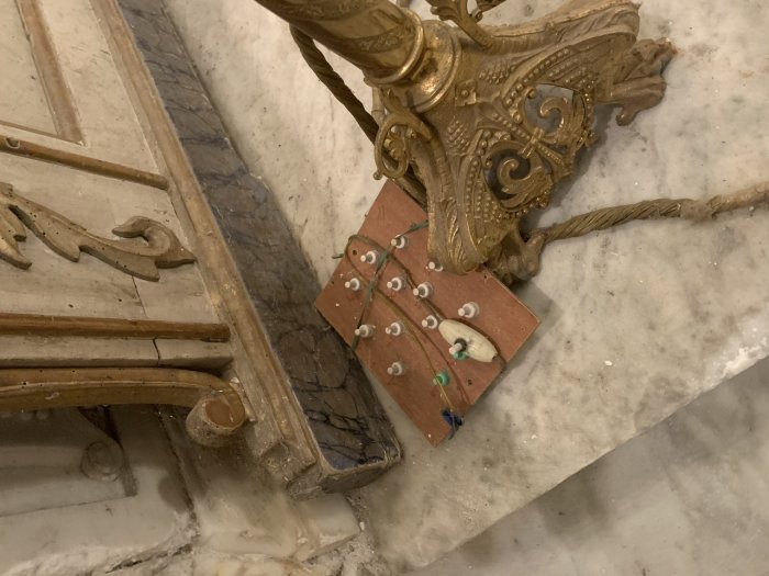 Detaljbild av en ovanlig förstärkning i en italiensk kyrka med vajrar och en träplatta fastsatta i marmor.