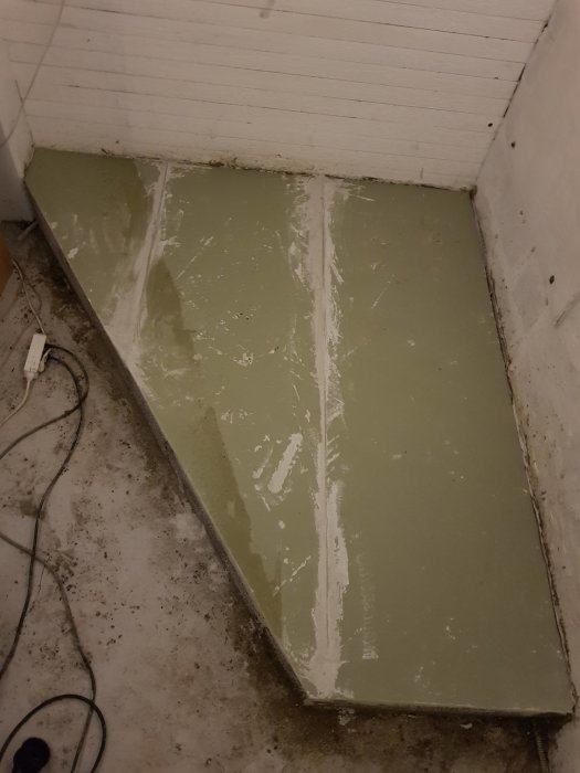 Hörn av nygjutet betongpodium i källare med släta ytor och vita väggar, förberett för kamininstallation.
