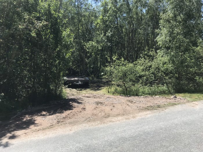 En nyanlagd provisorisk infart vid en skogstomt markerad med uppkörda högar av jord och grus.