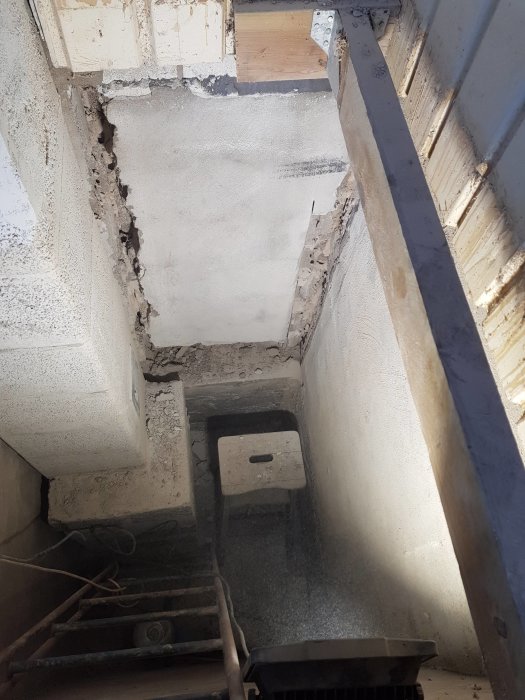 Vy ner i ett nästan tomt schakt med betongväggar och golv, där ett renoveringsprojekt för en kamin pågår.
