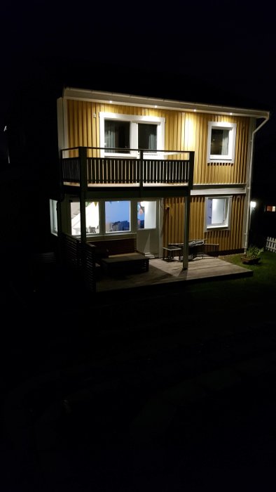 Ett hus om kvällen med belysning under takfoten som lyser upp fasaden och balkongen.