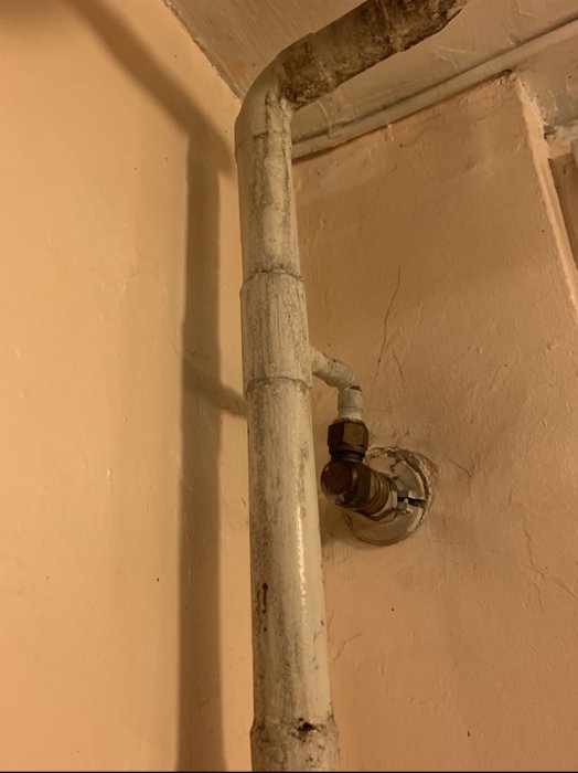 Ett målat vattenrör och ventilmekanism på en vägg som visar tecken på en ny målningsomgång men med äldre märken synliga.