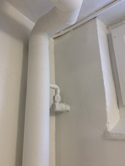 Nymålat rör och vägghörn i vitt med synliga spackelskarvar och ojämn yta som tecken på egen renovering.