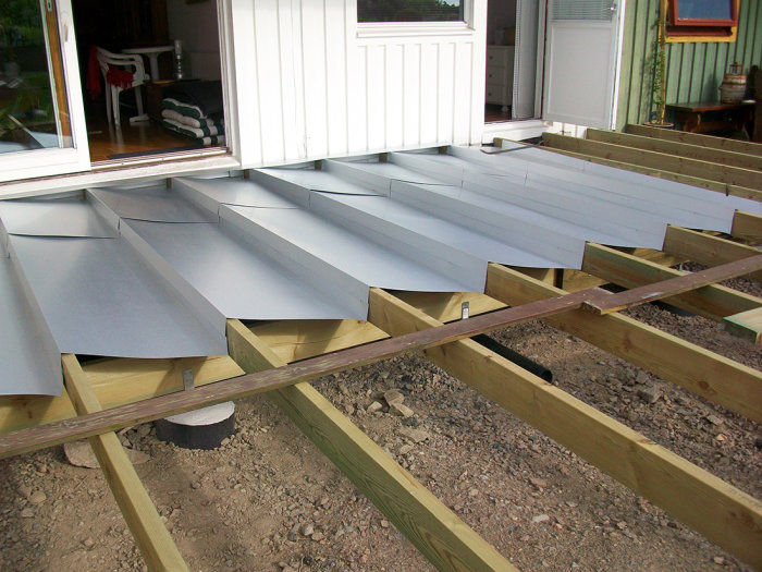 Installation av bockade avslutningsplåtar på träreglar för ett dragfritt golv vid husgrund.