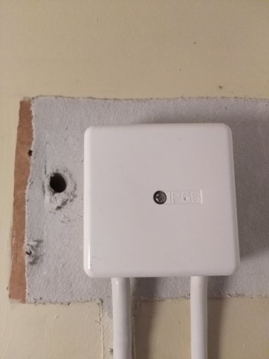 Eldistributionslåda på vägg med misstänkt asbestpapp synlig bakom och under lådan.