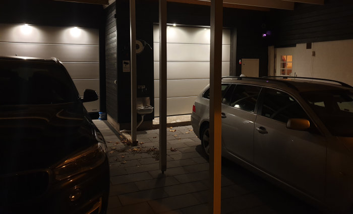 Upplyst garageuppfart med Multi hidealite lampor på en husvägg och två parkerade bilar på kvällen.