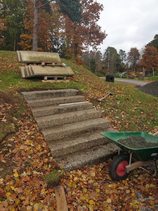 En nästan färdigställd trappa av återanvända trappsteg på en bergstomt omgiven av höstlöv, med en skottkärra full av grus.