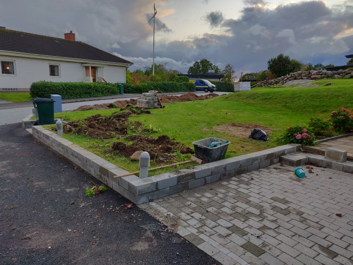 Nybyggd mur för häckrabatt vid uppfart med grävd mark och villa i bakgrunden.