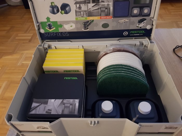 En öppen låda med produkter för träbehandling, inklusive flaskor med olja och polerpads, från varumärket Festool.