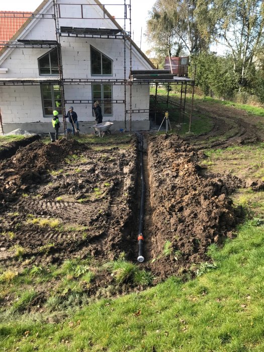 Hus under renovering med nytt tak och putsat fasad under arbete, arbetsfolk gräver för installationer.