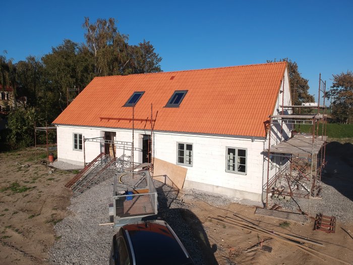 Hus med nytt rött tegeltak, påbörjad putsning på fasaden och byggnadsställningar runt huset.