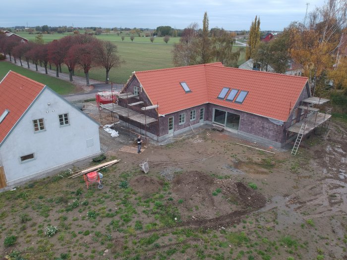 Nybyggd villa med komplett tak och påbörjad putsning, omgiven av ett lantligt landskap.