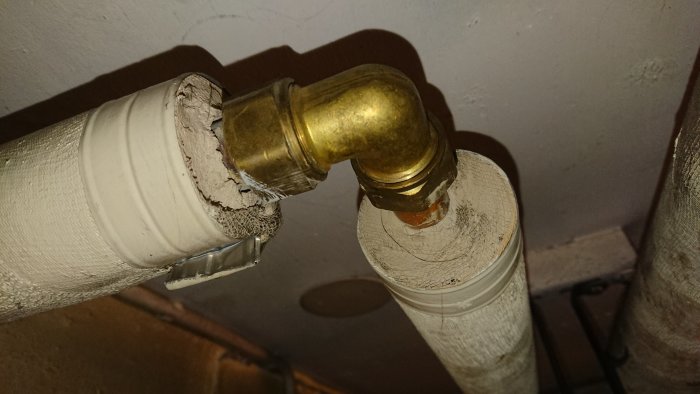 Vattenrör i källare med skadad, målad gipsisolering som kan innehålla asbest.