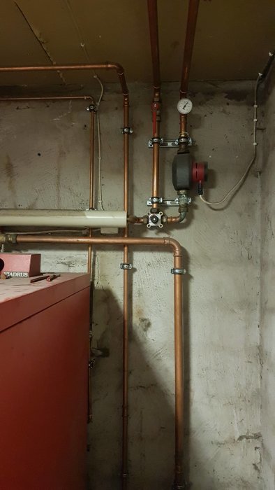 Kopparledningar och komponenter för värmesystem med ackumulatortank och tryckmätare i ett pannrum.