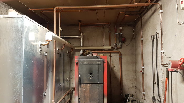 Ackumulatortank och kopparledningar i ett värmesystem med synlig Viadrus U22 panna.