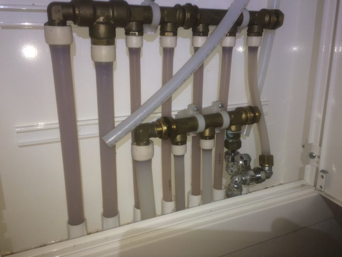 Trånga vattenledningar och kopplingar i ett badrumsskåp med tecken på kondens.