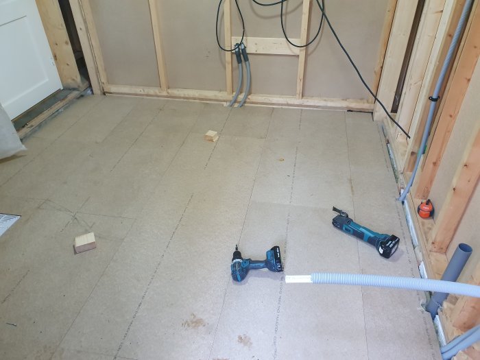 Renoveringsarbete med nya golvspån, reglar på vägg och verktyg på golvet.