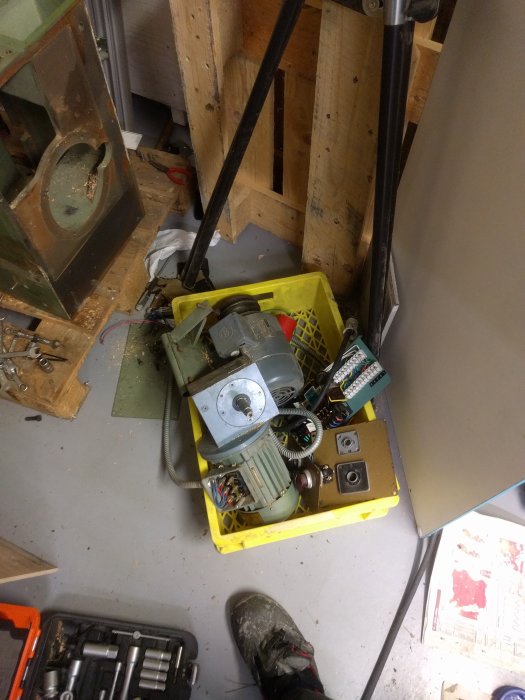 Gul verktygslåda med diverse verktyg och maskindelar på ett verkstadsgolv.