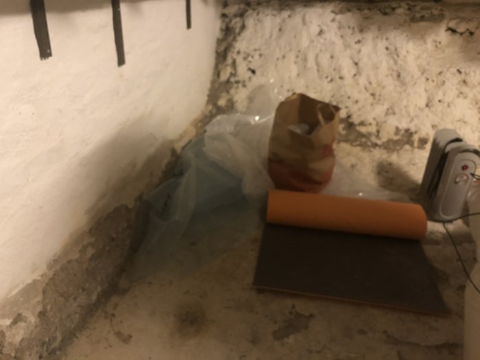 Gammal källare med murad vägg ovanför synligt stengrund, renoveringsmaterial på golvet, tecken på fukt eller råhet.