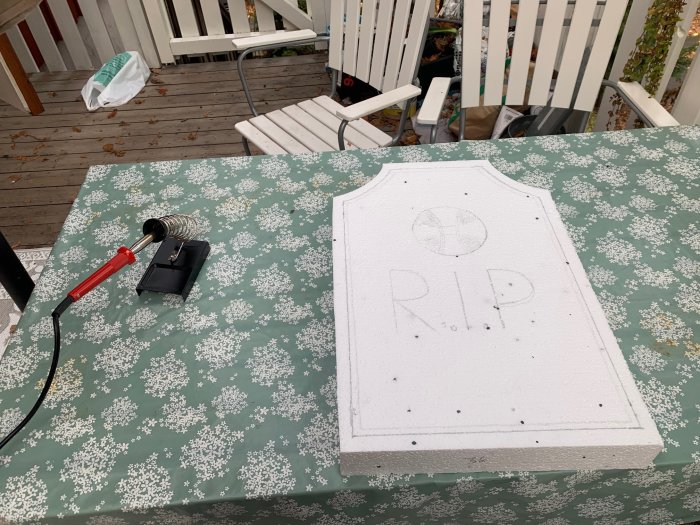 Hemmagjord gravsten av cellplast med "R.I.P" inskription på ett bord med lödkolv för utformning.