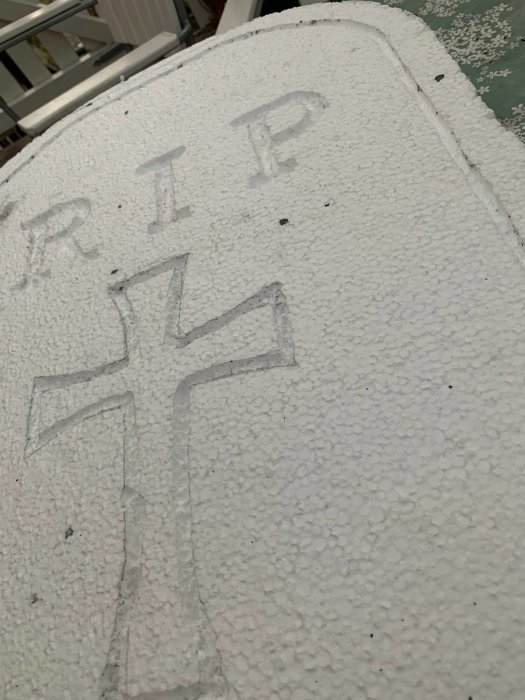 Hemmagjord gravsten av cellplast med inskriptionen "RIP" och ett kors, i arbete för Halloween.