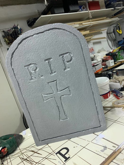 Handgjord gravsten i cellplast för Halloween med inskriptionen "RIP" och ett kors, målad grå och åldrad.