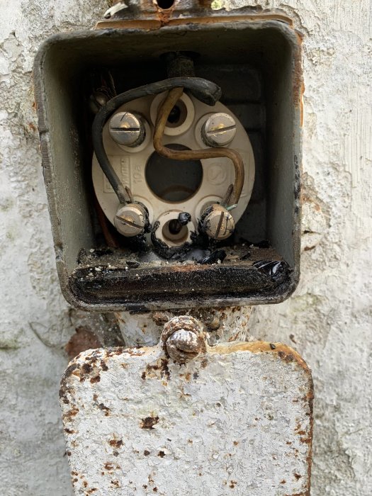 Gammal elektrisk dosa med två trådar, korroderad med synlig jordkabel.