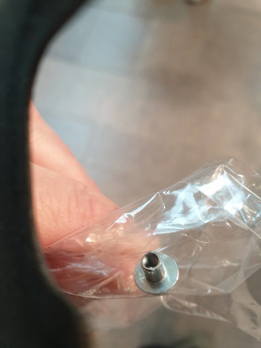 Närbild av en gängad metallskruv med insida synlig, hålls framför en genomskinlig plastpåse.