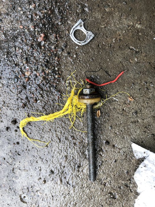 Orenheter i grus med en stor skruv, kapsyler och gula plasttrådar på ett vått underlag.