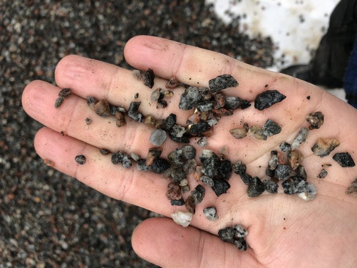 En hand öppen som visar en blandning av små stenar och grus, en del för små och med otvättade fragment.