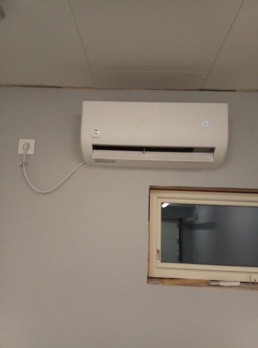 Luftkonditioneringsenhet installerad på en garagevägg ovanför ett fönster.
