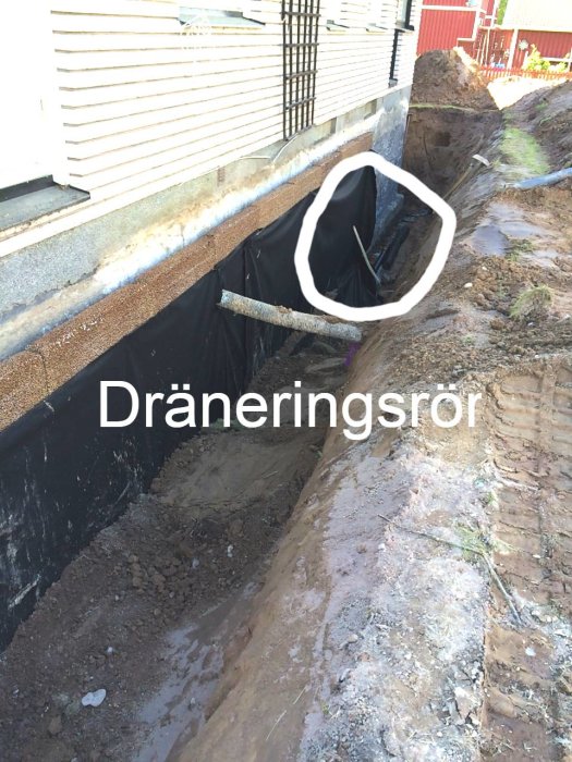 Dräneringsrör längs ett hus under byggnadsarbeten med en grävd dräneringsdike synlig.