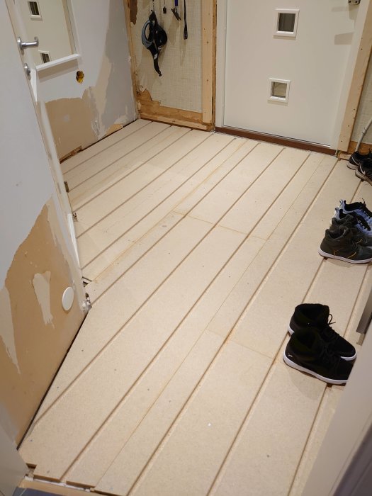 Nyinstallerade golvspånplattor i ett rum under renovering med väggdelvis avlägsnad och skor på golvet.