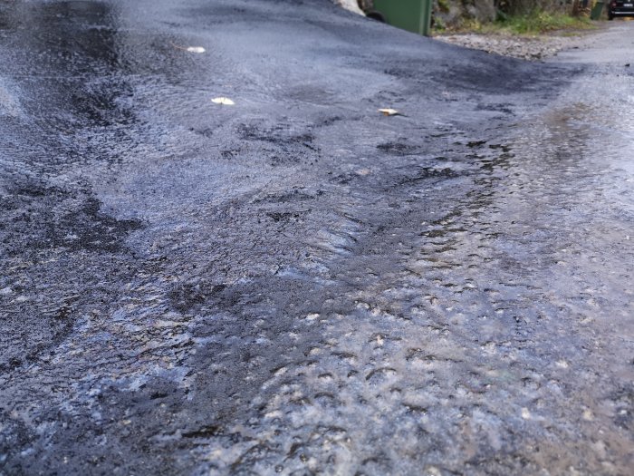 Asfaltsuppfart med ny lappning där klister och sand är applicerat under regniga förhållanden.