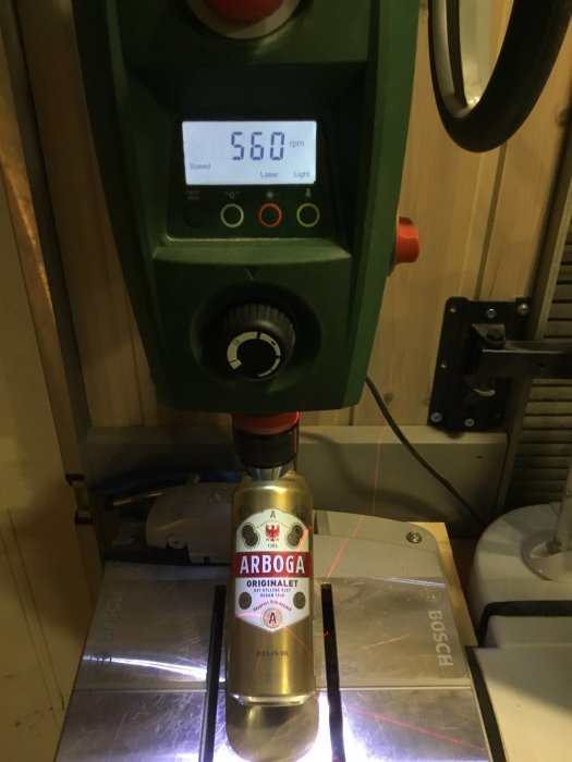 Ölflaska märkt "ARBROGA" under borrmaskin med displayen visande 560 rpm och laserkors på flaskan.