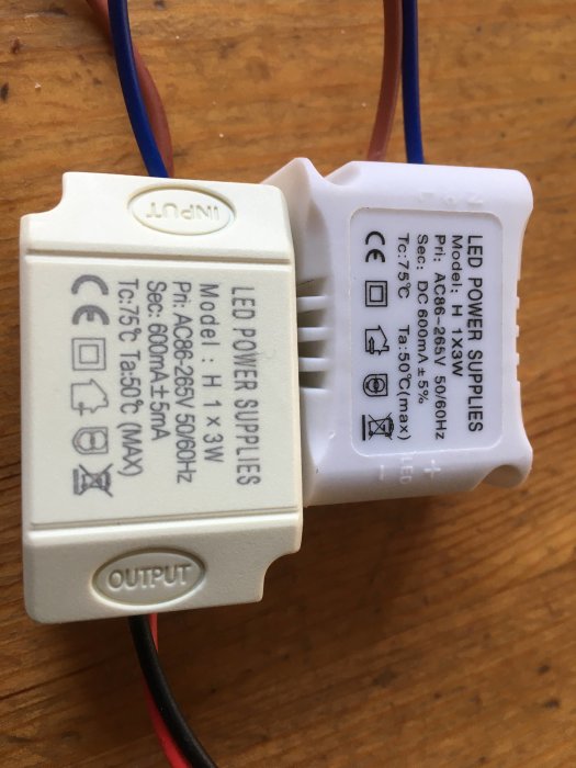 En LED-drivare med ingångs- och utgångskablar synliga, placerad på ett träbord.