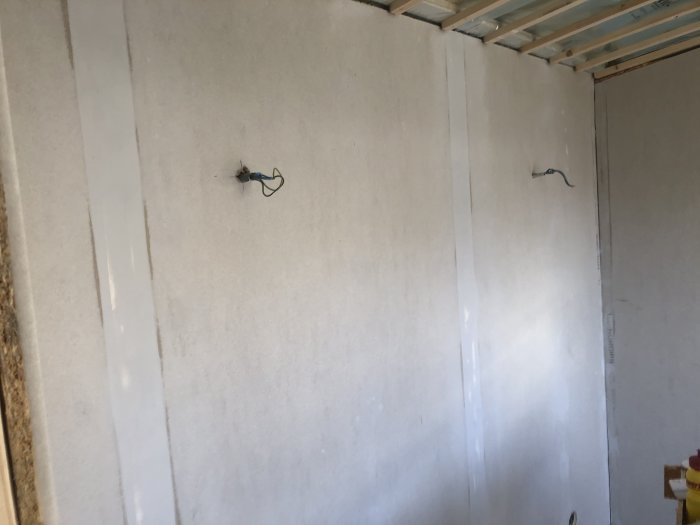 Rum under renovering med oslipade väggar, synliga elledningar och takbjälkar.
