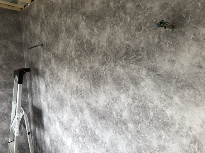 Nyinstallerad enkel betongmönstrad tapet på vägg med eluttag och stege, klart för ytterligare renovering.