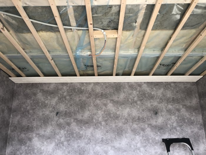 Oavslutat tak med träreglar och isolering samt vägg med ny grå betongmönstrad tapet och takarmaturförberedelser.