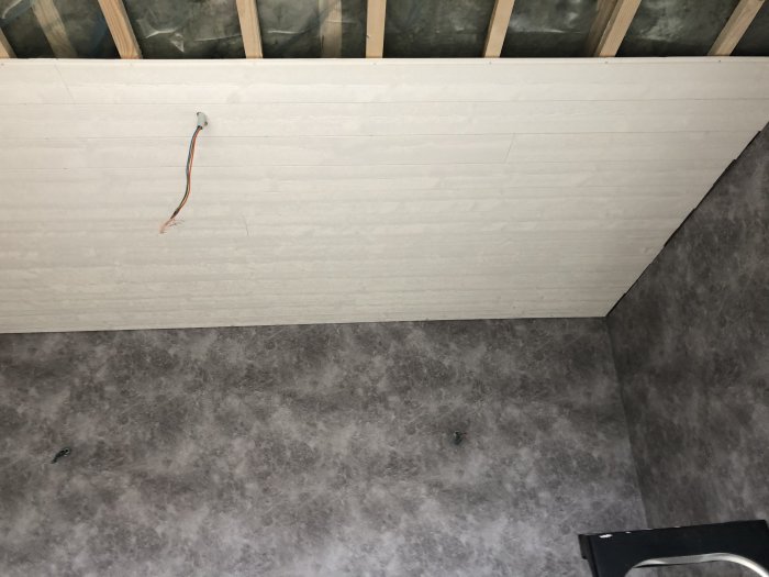 Nyinstallerad paneltak och betongmönstrad tapet på väggar med synlig elledning och två vägguttag.