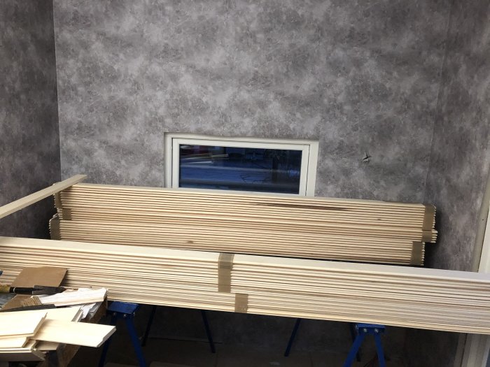 Nyinstallerad grå betongmönstrad tapet med bastupanel staplade framför i ett renoveringsprojekt.