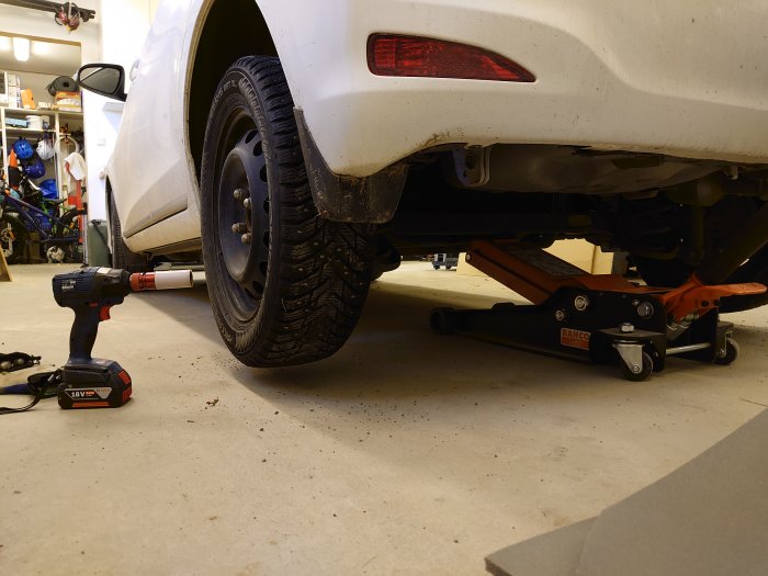 Bil upplyft med domkraft och en löstagbar mutterdragare på garagegolvet.