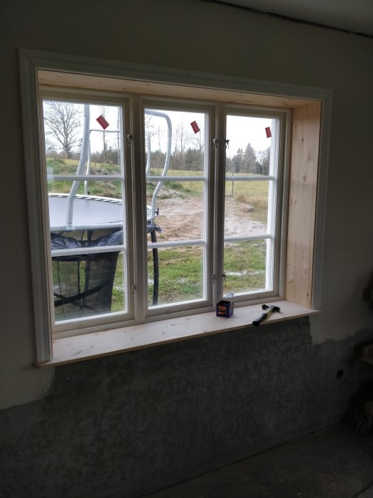 Nyinstallerade fönster med skyddsfolie kvar på rutorna och nymonterad fönstersmyg, i ett rum under renovering.