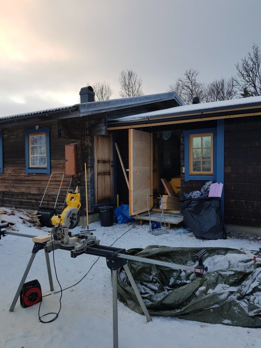 Isolerad provisorisk OSB-dörr på bygge under vintern, kapsåg i förgrunden, snöigt underlag.