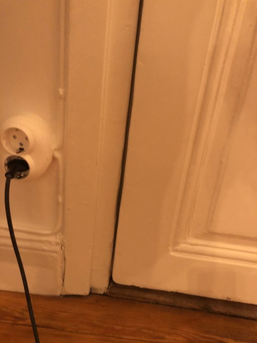 Dörr som inte stänger sig ordentligt nedtill, vägguttag och sladd synliga.