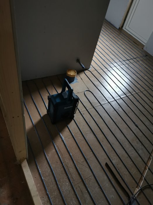 Golvvärmeinstallation med värmeslingor på golv och en värmefläkt står i ett rum under renovering.