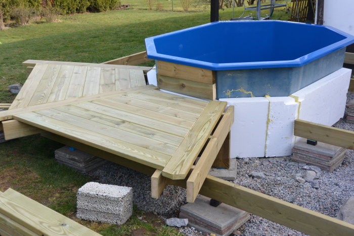 En oktagonformad pool med blå insida, delvis klädd med trätrall och vit isolering synlig vid grunden.