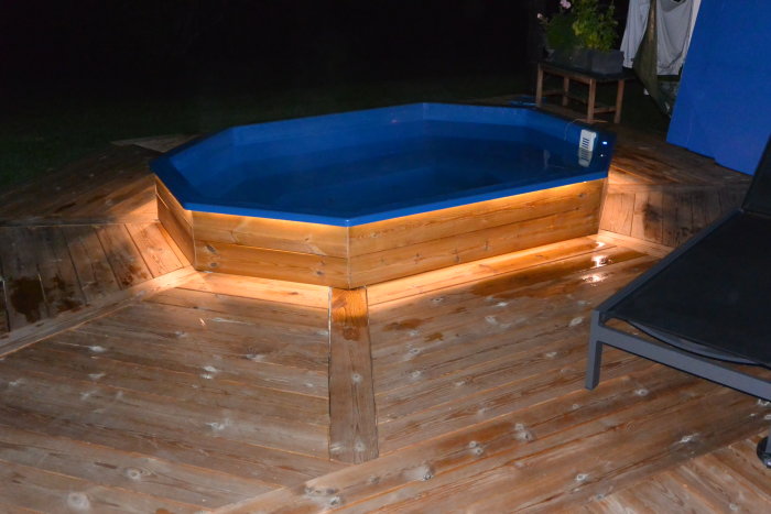 Ett åttkantigt badkar omgivet av en trätrall, belyst med spotlights på natten, exemplifierar en hembad installation.