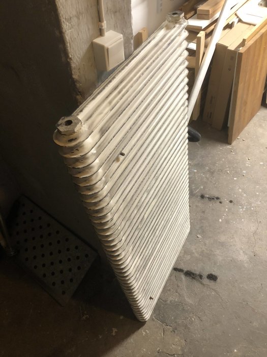 Gammal sektionsradiator står lutad mot en vägg i förberedelse för installation.